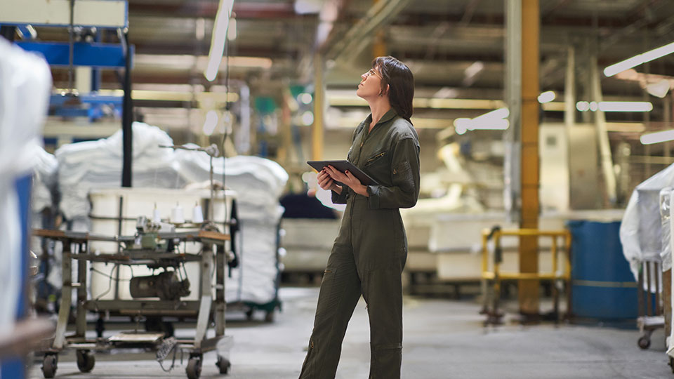 A woman in coveralls holding a tablet in a warehouse