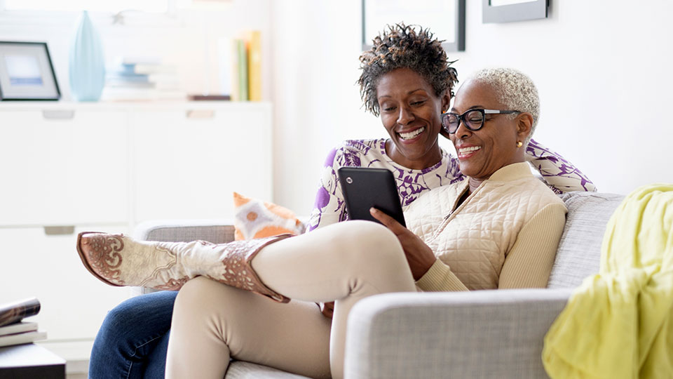 Two women sit on a couch together looking a tablet